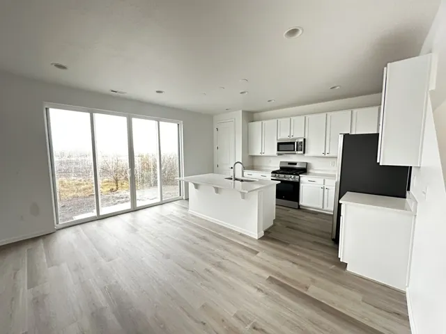 Open concept kitchen with white cabinetry, stainless steel appliances, and a central island with a sink