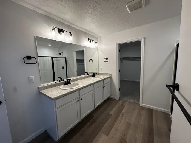 Dual vanity with undermount sinks, wood-finish flooring, a full-width mirror, and a walk-in shower with a sliding glass door