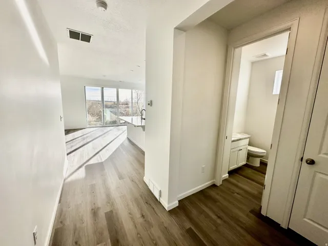Wood-finish flooring throughout, bright white walls, modern recessed lighting, full-height windows, and a powder room with a vanity