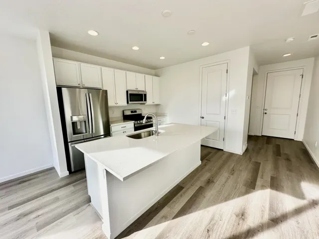Kitchen featuring white cabinetry, stainless steel appliances, a center island with a sink, and wood-finish flooring