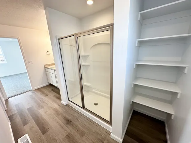 Wood-finish flooring, built-in shelving, glass-enclosed shower, single vanity with integrated sink, and recessed lighting