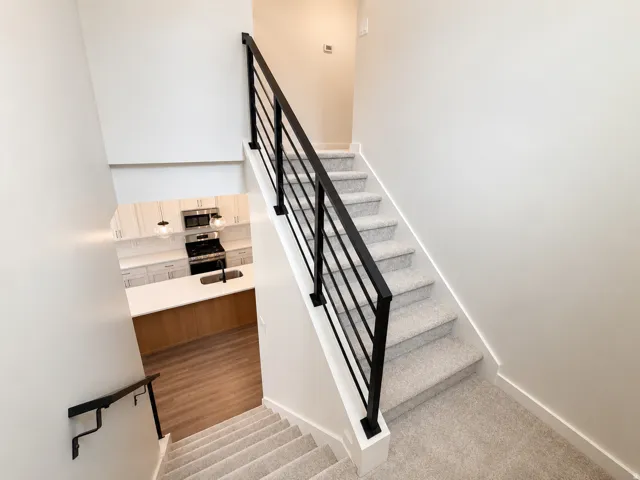 Carpeted staircase with contemporary metal railings and a clear sightline to the kitchen below