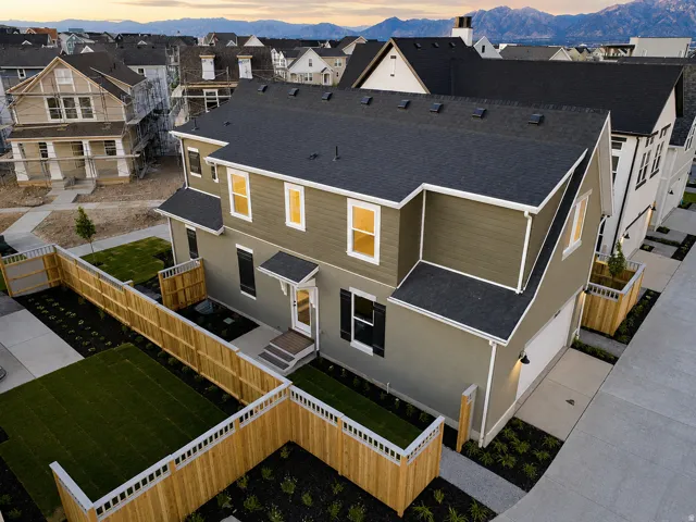 Contemporary two-story residence featuring a dark gray shingle roof, two-tone exterior siding, a private fenced yard with artificial turf, and an attached garage