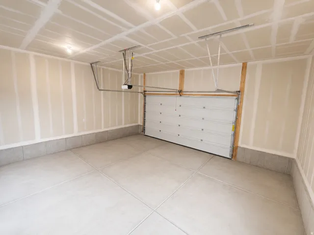 Spacious garage featuring a concrete floor, light-toned walls, overhead lighting, and a white panel garage door with an automatic opener