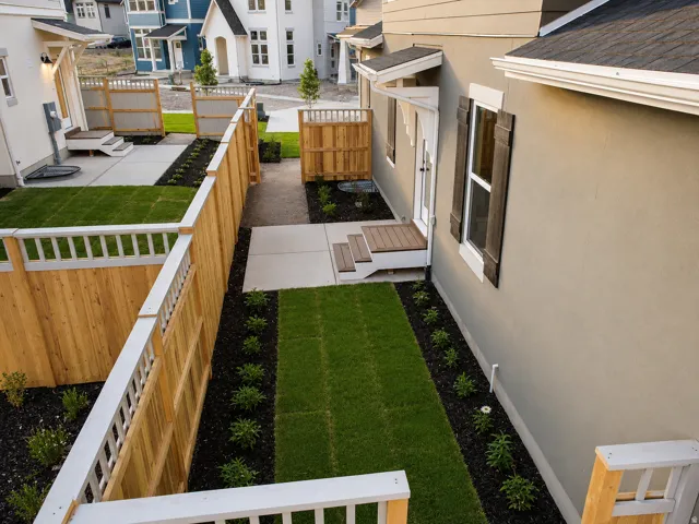 Private side yard featuring new sod, landscaped beds with dark mulch, and a concrete patio
