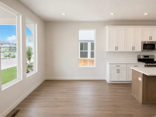 Open-concept living space with wood-finish flooring, white cabinetry, stainless steel appliances, and abundant natural light from multiple windows