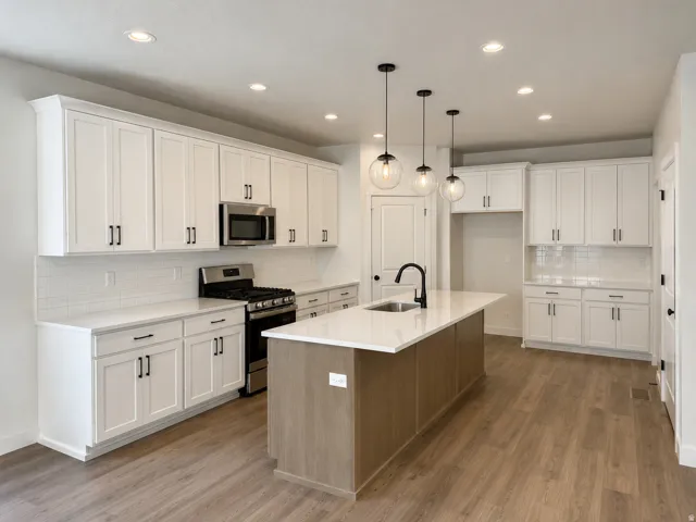 Kitchen featuring white shaker cabinetry, stainless steel appliances, a center island with sink, white countertops, and wood-finish flooring