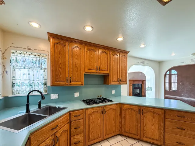 Kitchen featuring wood-finish cabinetry, light blue countertops, a dual basin stainless steel sink with a matte black faucet, and a gas cooktop
