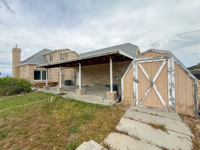 Brick exterior home featuring a covered patio, an exterior chimney, and a storage shed