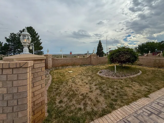 Landscaped yard featuring brick walls, integrated lantern lighting, a patterned brick walkway, and a circular planting bed with a mature tree