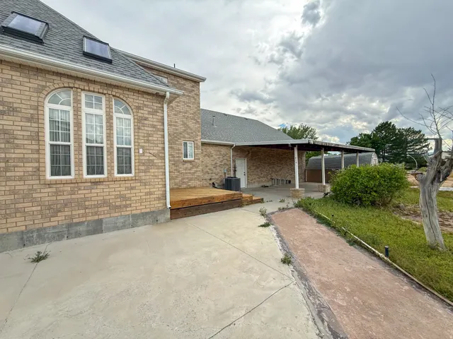 Brick exterior featuring a wooden deck, covered patio, and concrete hardscaping