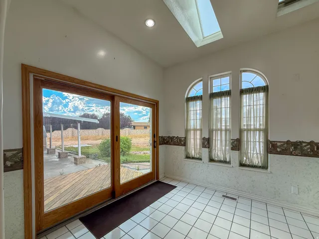 Spacious room featuring white tile flooring, vaulted ceiling with recessed lighting and a skylight, wood-framed sliding glass doors, and three arched windows