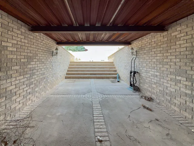 Sheltered outdoor space featuring light-colored brick walls, a wood-finish ceiling, and concrete flooring with brick accents