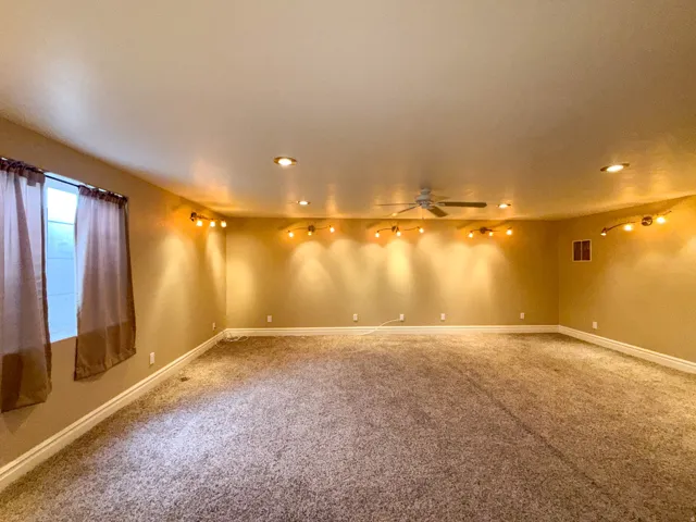 Spacious room featuring neutral carpeting, recessed ceiling lighting, track lighting accents, a ceiling fan, and a window with white trim