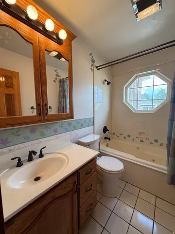 Bathroom featuring a cream-colored built-in jetted tub, an octagonal window, and a wood-finish vanity with a white countertop and oval sink