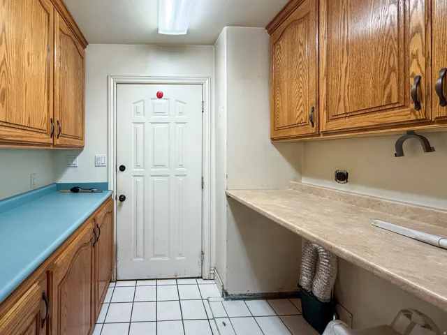 Utility room featuring white square tile flooring, wood cabinetry with dark hardware, and a solid white paneled door