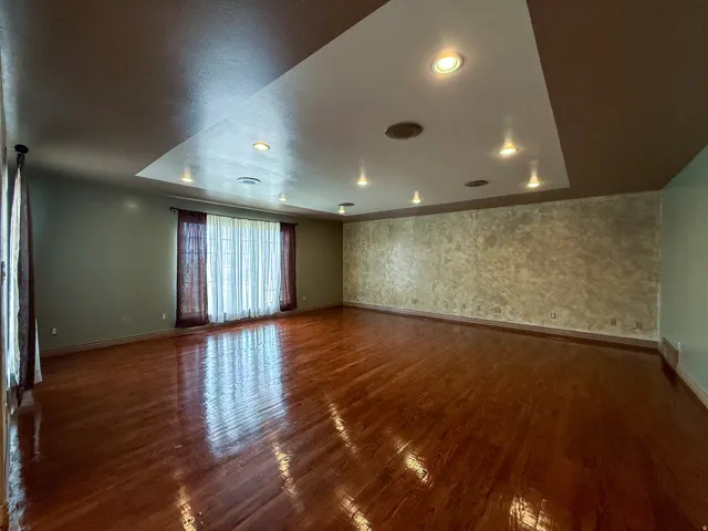 Spacious room featuring polished wood-finish flooring, a tray ceiling with recessed lighting, and a textured accent wall
