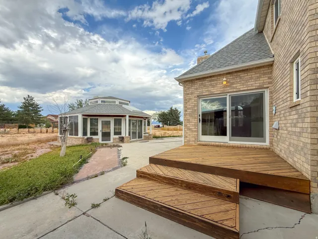 Exterior brick residence featuring a multi-level wood deck, sliding glass door access, and a separate octagonal sunroom with multiple glass doors and transom windows