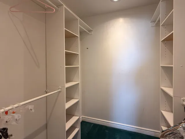 Walk-in closet featuring white built-in shelving units, integrated hanging rods, recessed ceiling lighting, and a dark green carpeted floor