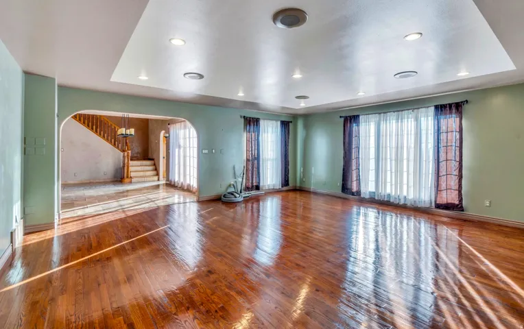 Expansive living area featuring wood-finish flooring, recessed lighting, a tray ceiling, and large windows with privacy sheers
