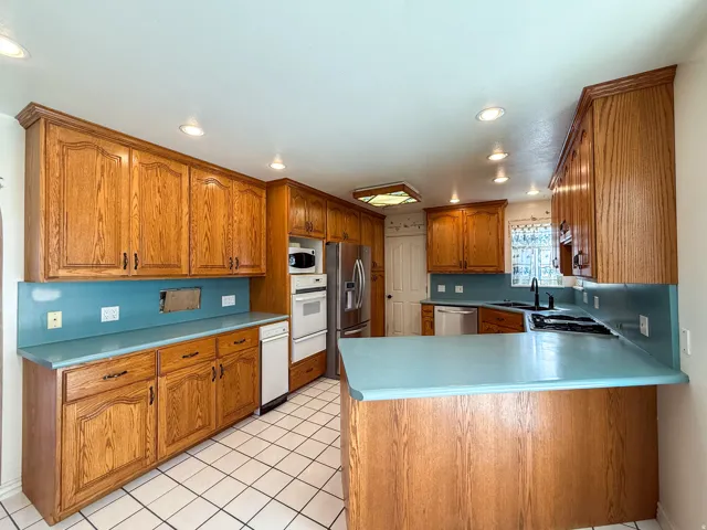Kitchen featuring wood-finish cabinetry, light blue countertops, white tile flooring, and recessed lighting