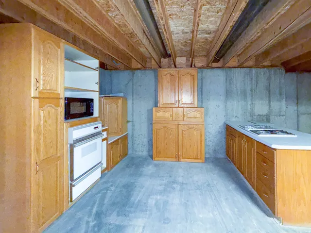 Unfinished basement space featuring a built-in oven, microwave, and cooktop