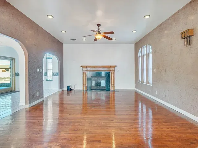 Spacious interior featuring wood-finish flooring, a decorative fireplace with a carved wood mantel, and arched window openings