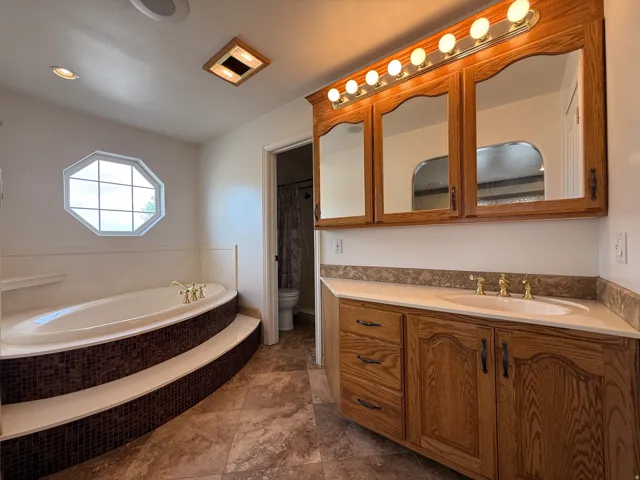 Bathroom featuring a built-in soaking tub with mosaic tile surround, an octagonal window, and a wood vanity with integrated sink and storage