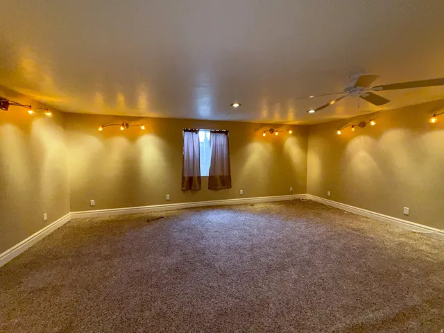 Spacious room featuring broadloom carpeting, a single window with curtain treatments, recessed lighting, track lighting, and a ceiling fan