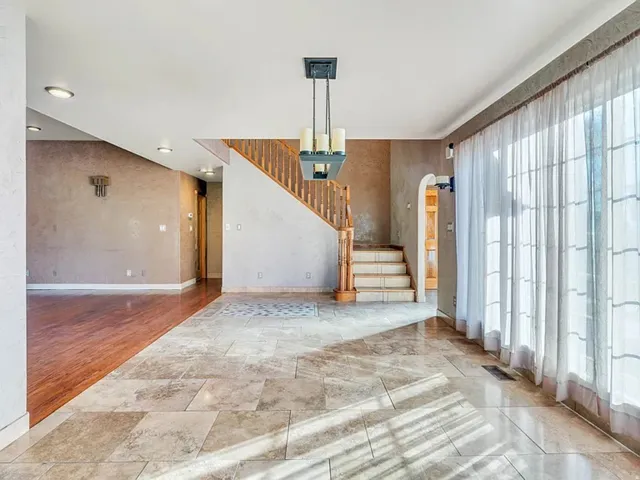 Spacious interior featuring varied flooring, a wooden staircase with railing, an arched doorway, recessed lighting, and a modern chandelier