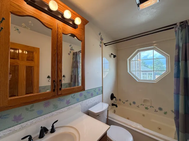 Bathroom featuring an octagonal window, a built-in jetted tub, and a wood-finish medicine cabinet with integrated lighting
