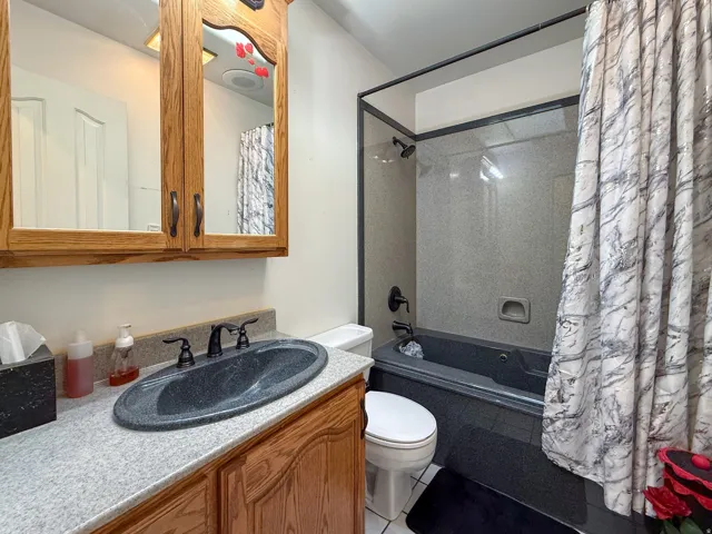Bathroom featuring a jetted tub, a built-in shower, a light-toned countertop, and an oak vanity with storage