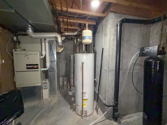 Basement utility area featuring a furnace, hot water heater, ductwork, exposed ceiling joists, and a water treatment system
