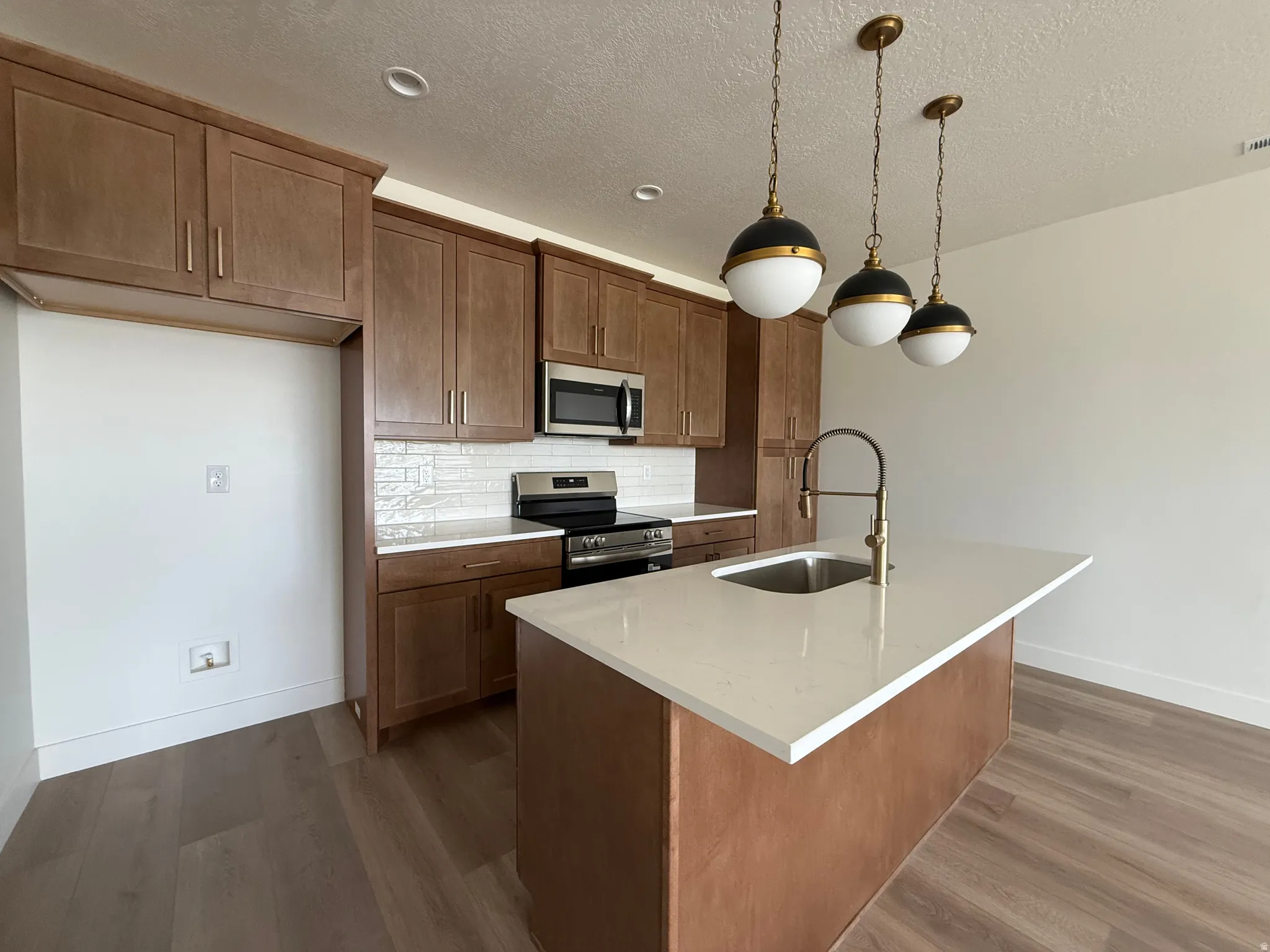 Contemporary kitchen featuring wood-finish cabinetry, stainless steel appliances, white subway tile backsplash, and a kitchen island with a single-basin sink