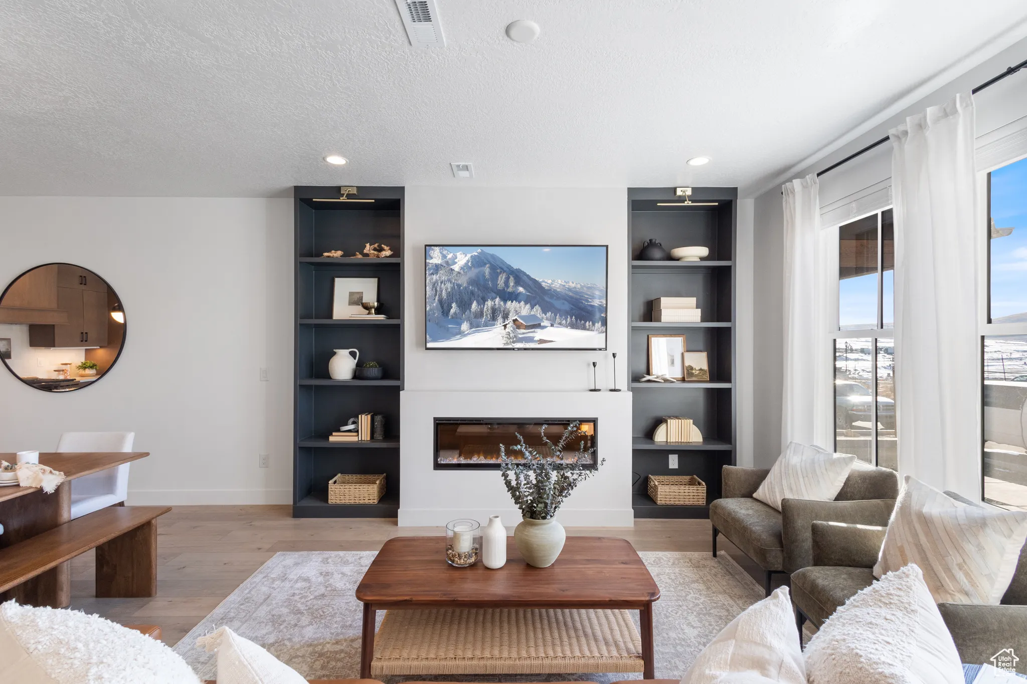 Integrated fireplace with custom built-in shelving, recessed lighting, wood-finish flooring, and expansive windows