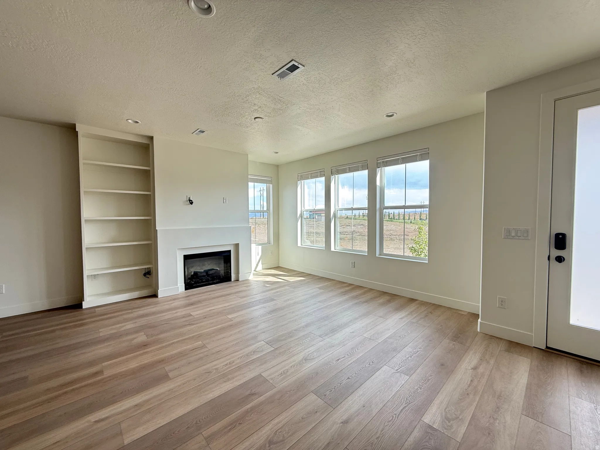 Wood-finish flooring throughout, built-in shelving, fireplace with mantel, recessed lighting, and a frosted glass-paneled door