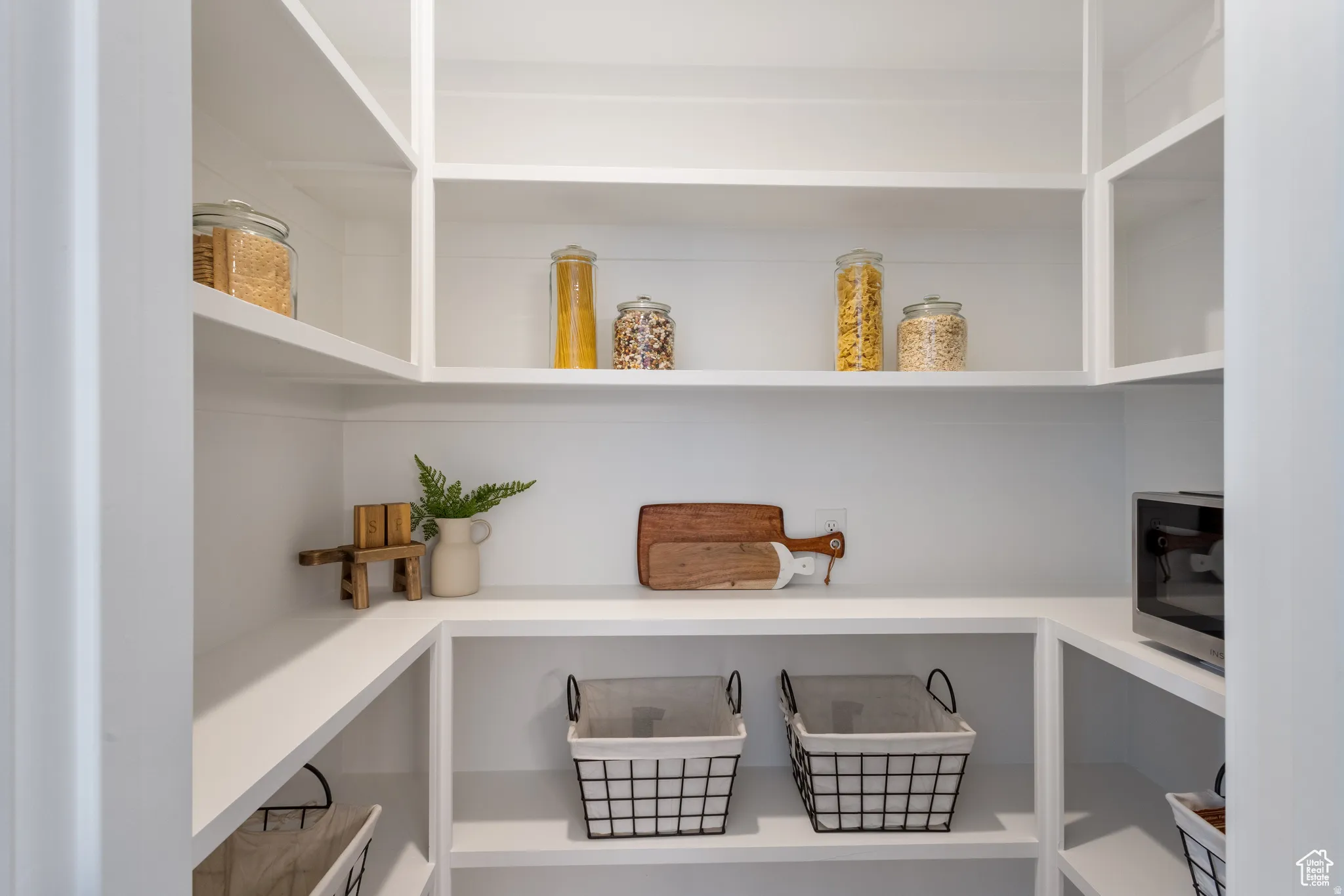 Walk-in pantry featuring extensive built-in shelving, white finishes, and an integrated power outlet