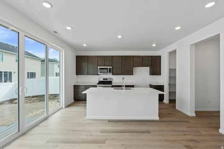 Open-concept kitchen with a central island, recessed lighting, wood-finish flooring, dark cabinetry, and white countertops