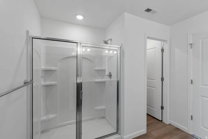 Shower enclosure with clear glass doors and chrome hardware, integrated shelving, recessed lighting, and wood-finish flooring