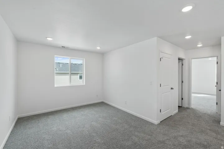 Recessed ceiling lighting, a window with exterior views, white walls, gray carpeting, and a white paneled door