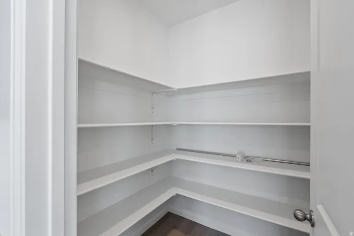 Corner pantry with multiple white shelves and wood-finish flooring