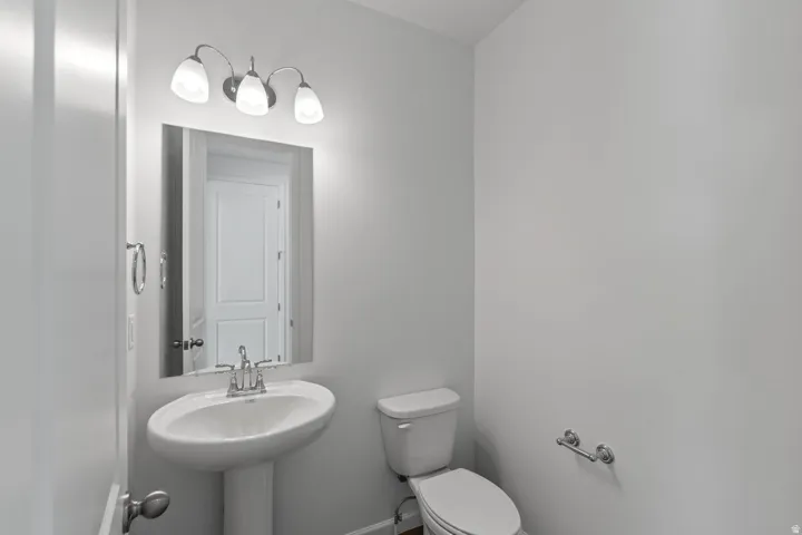 Pedestal sink with chrome faucet, wall-mounted mirror, three-light vanity fixture, and white toilet