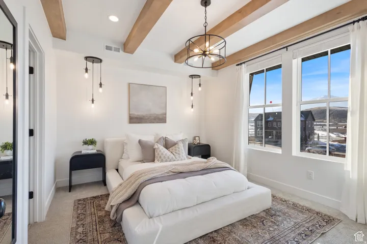 Spacious room featuring exposed wood-finish ceiling beams, two large windows, a black drum chandelier, and two pendant light fixtures