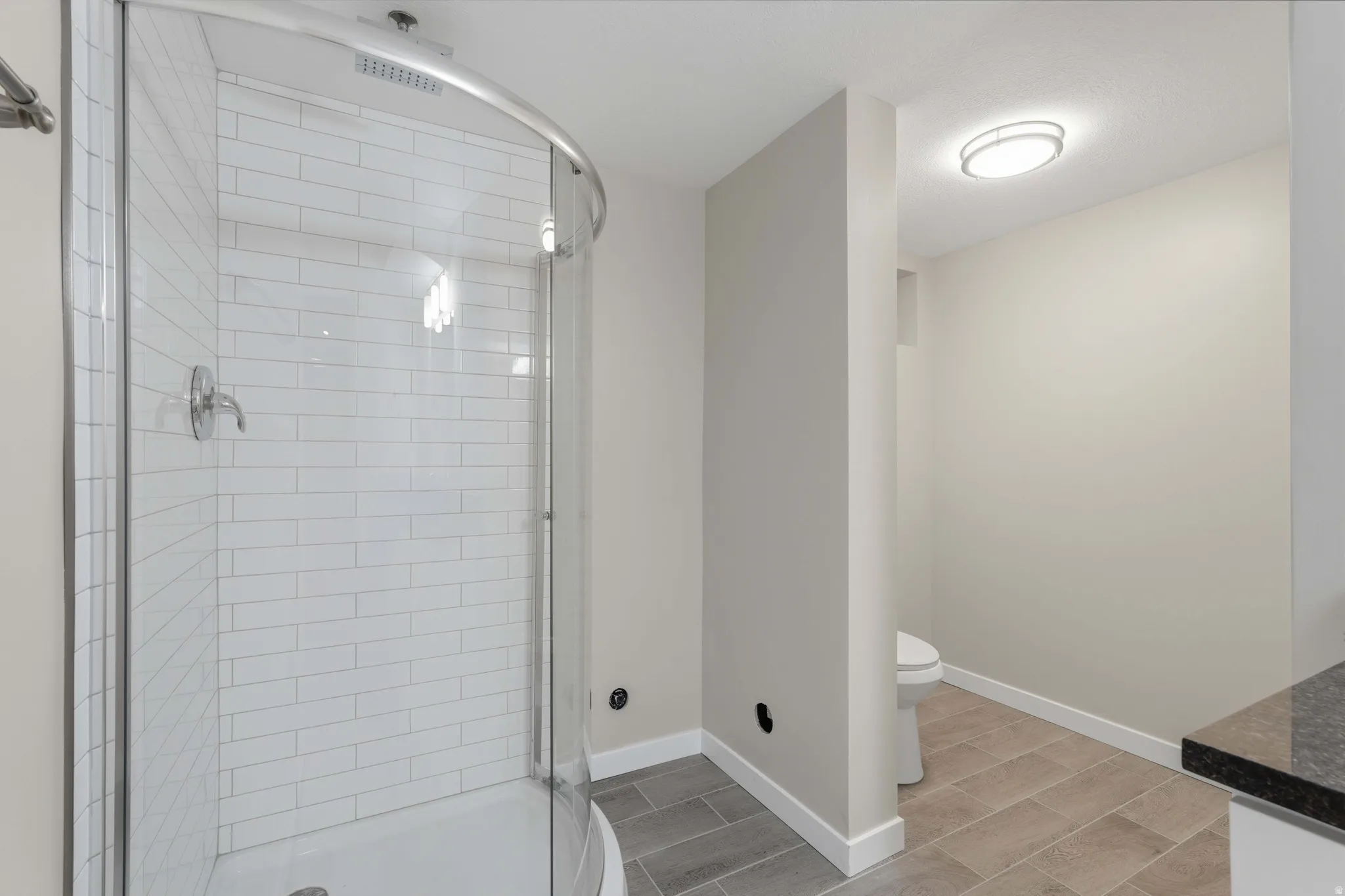 Curved glass shower enclosure with subway tile surround and chrome fixtures