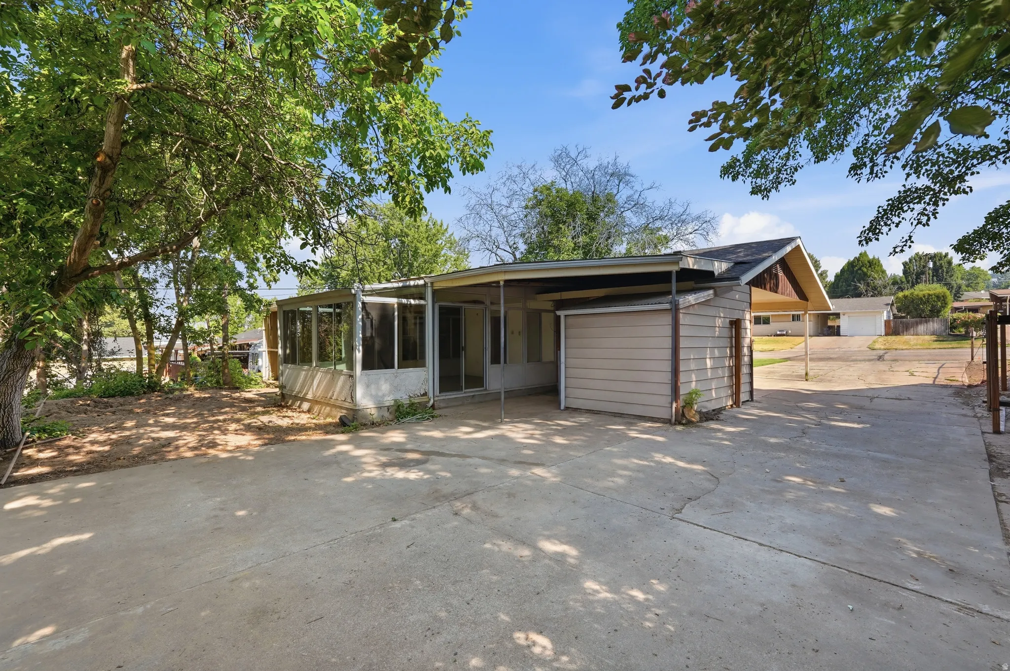 Expansive concrete driveway with mature trees, screened porch, and attached storage shed