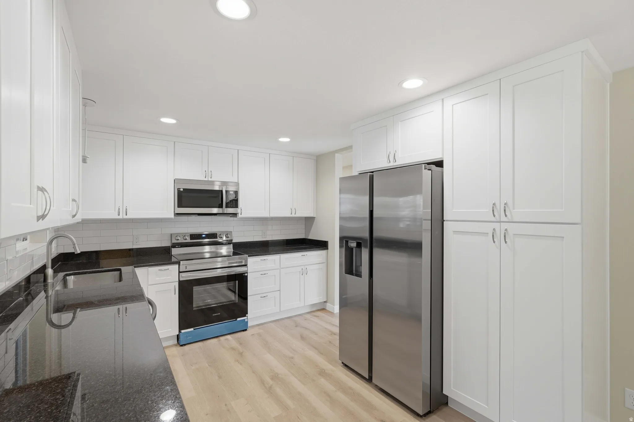 Modern kitchen featuring white shaker-style cabinetry, dark stone countertops, and stainless steel appliances
