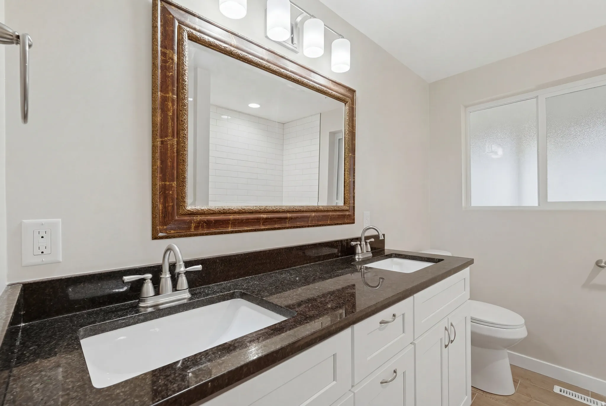 Dual vanity with dark stone countertop, white shaker cabinetry, and brushed nickel fixtures