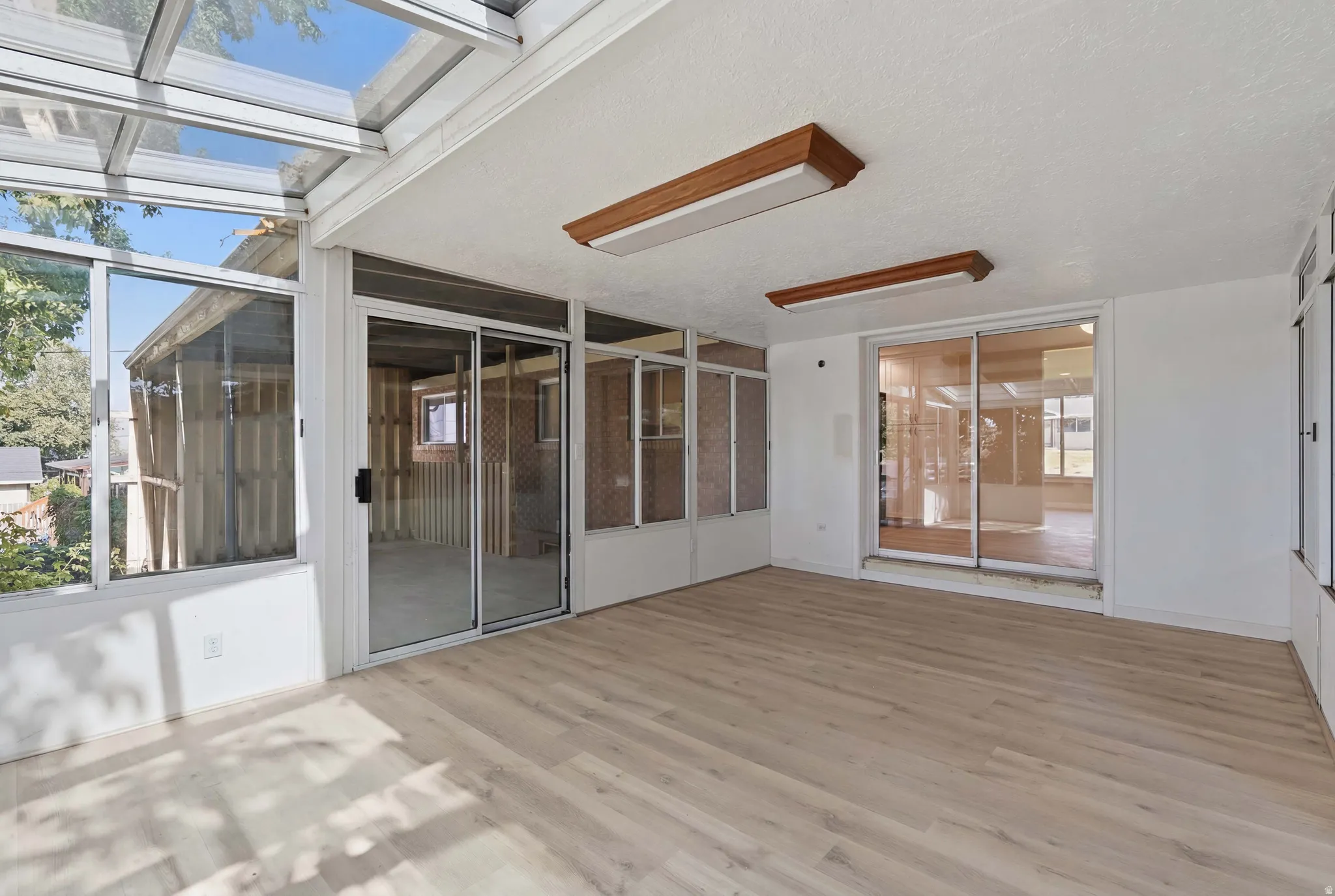 Spacious sunroom featuring a glass panel roof, multiple large windows, light wood-finish flooring, and recessed ceiling lighting