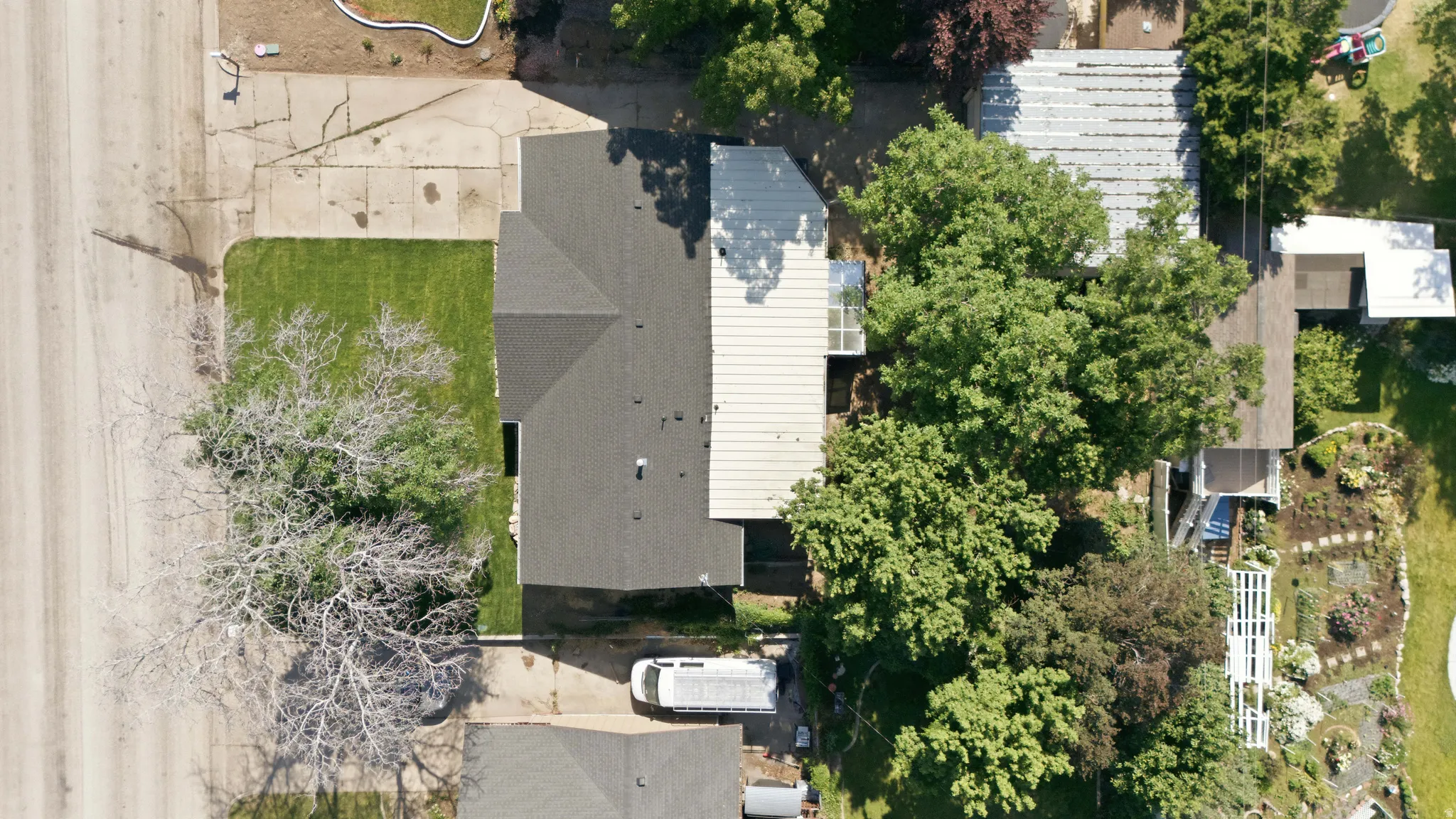 Property featuring a dark shingle roof, green lawn, and mature trees