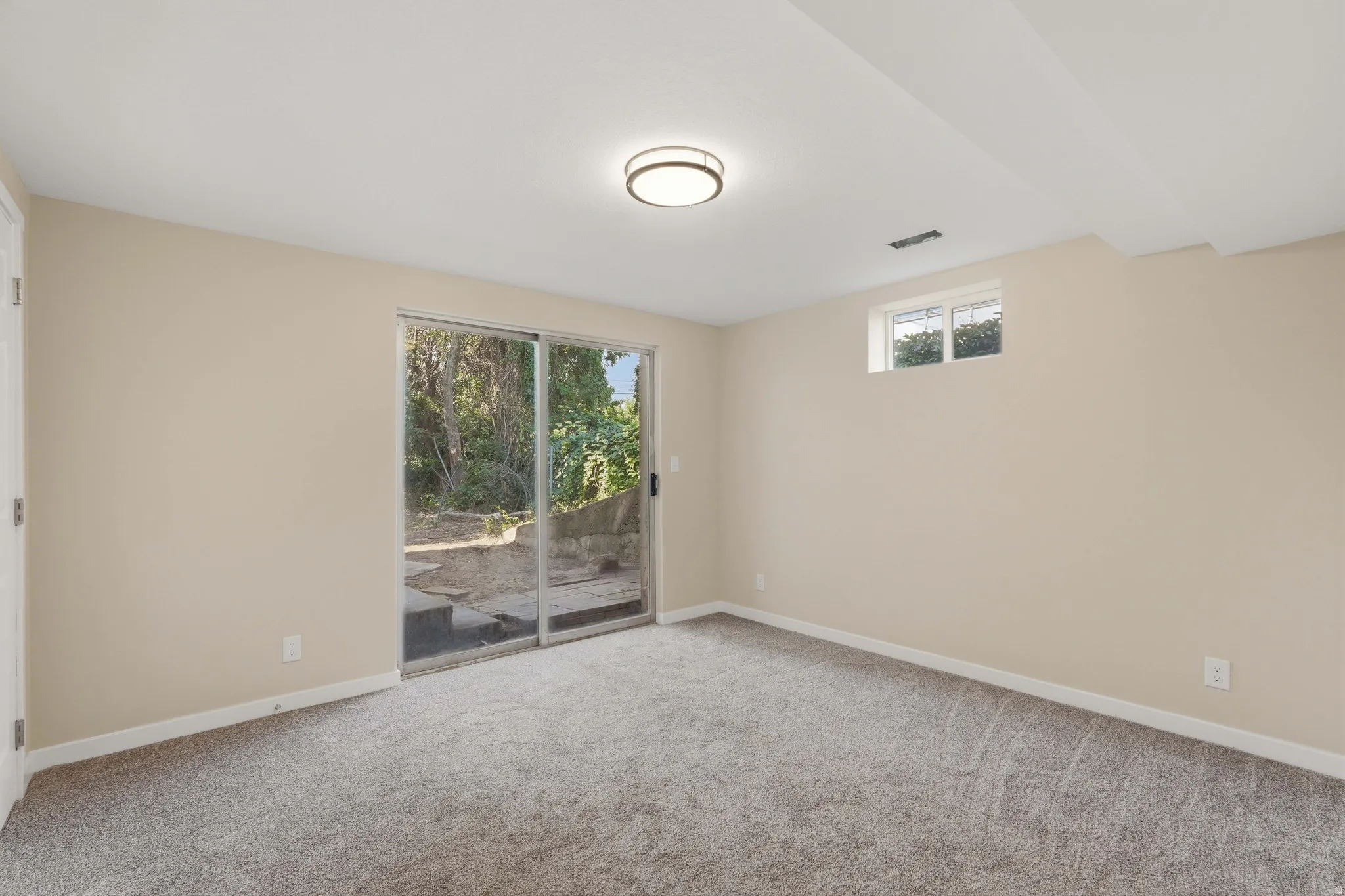 Spacious room featuring light beige walls, gray carpet flooring, and a contemporary flush-mount ceiling light